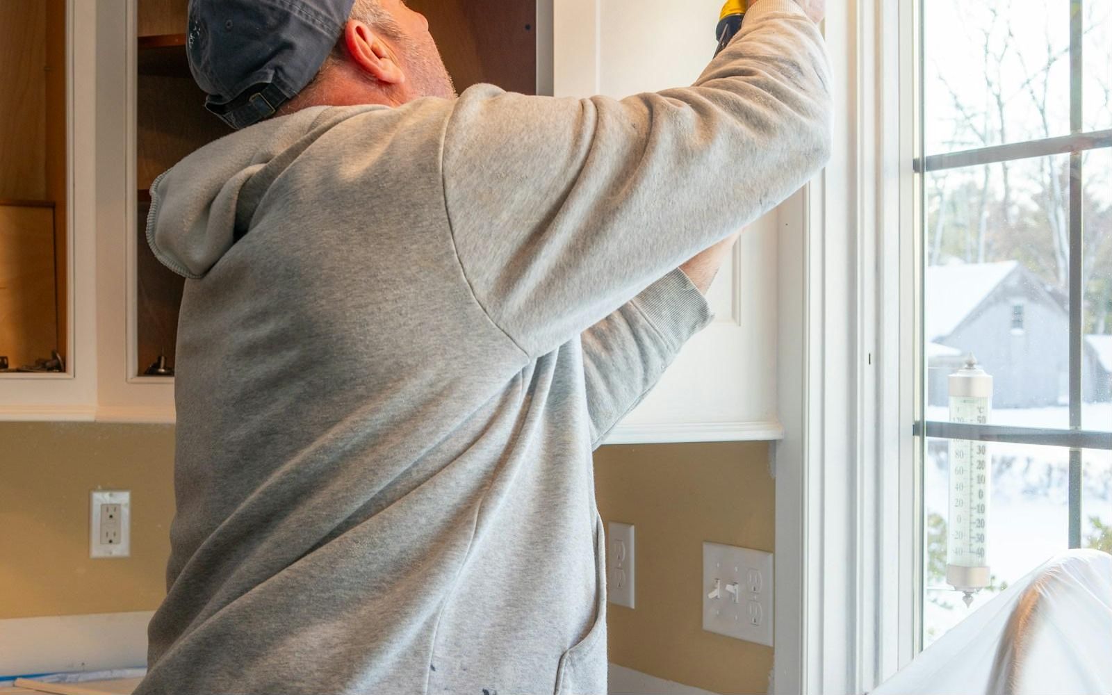 Installer mounting a cabinet with a drill
